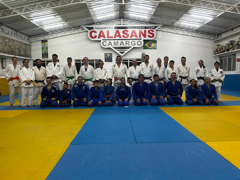 Turma e professores da Academia Calasans Camargo reunidos no tatame, sob o letreiro