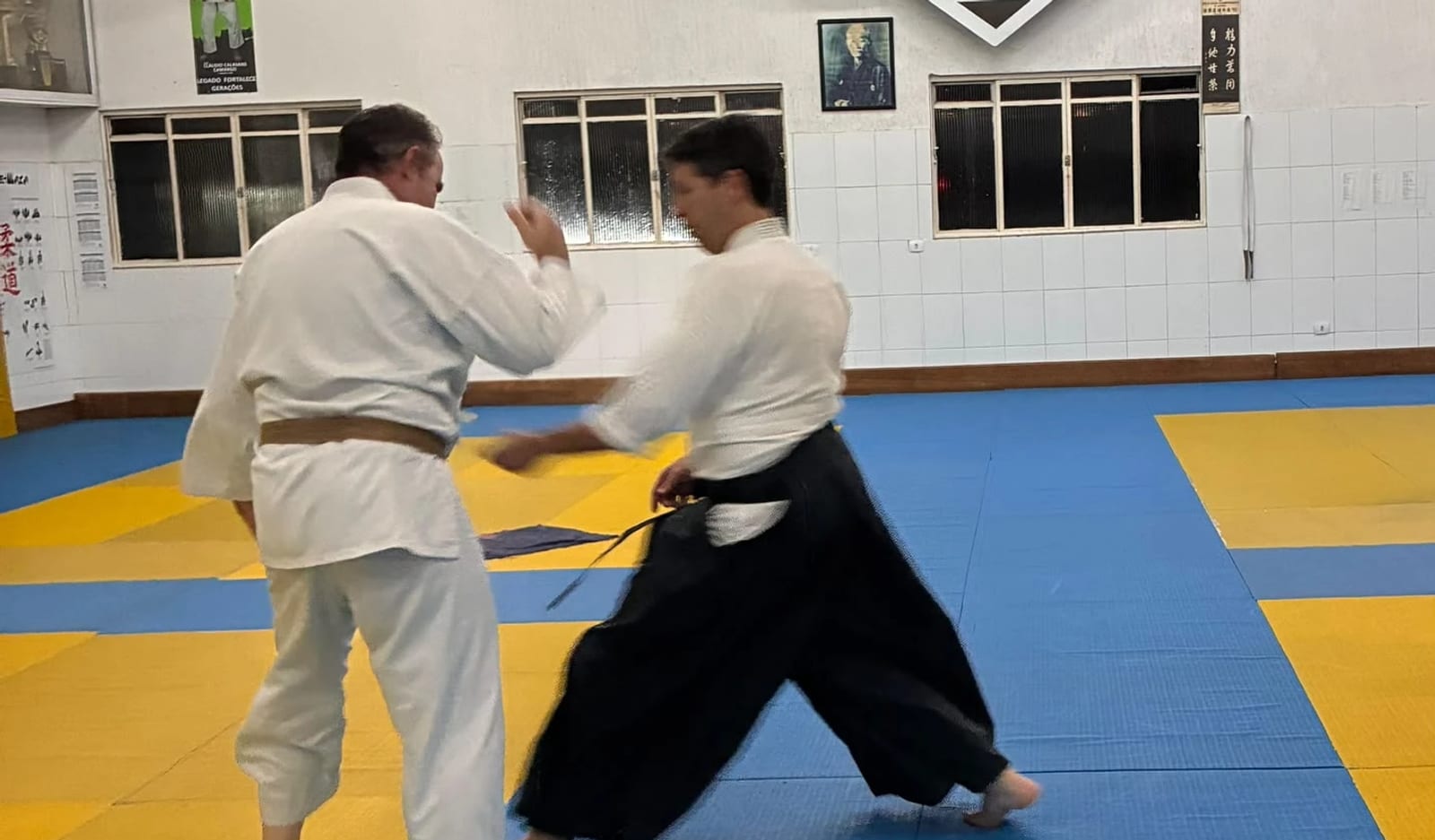 Aula de Aikidô na Academia Calasans Camargo — projeção com uke de judogi e aikidoísta de hakama no tatame